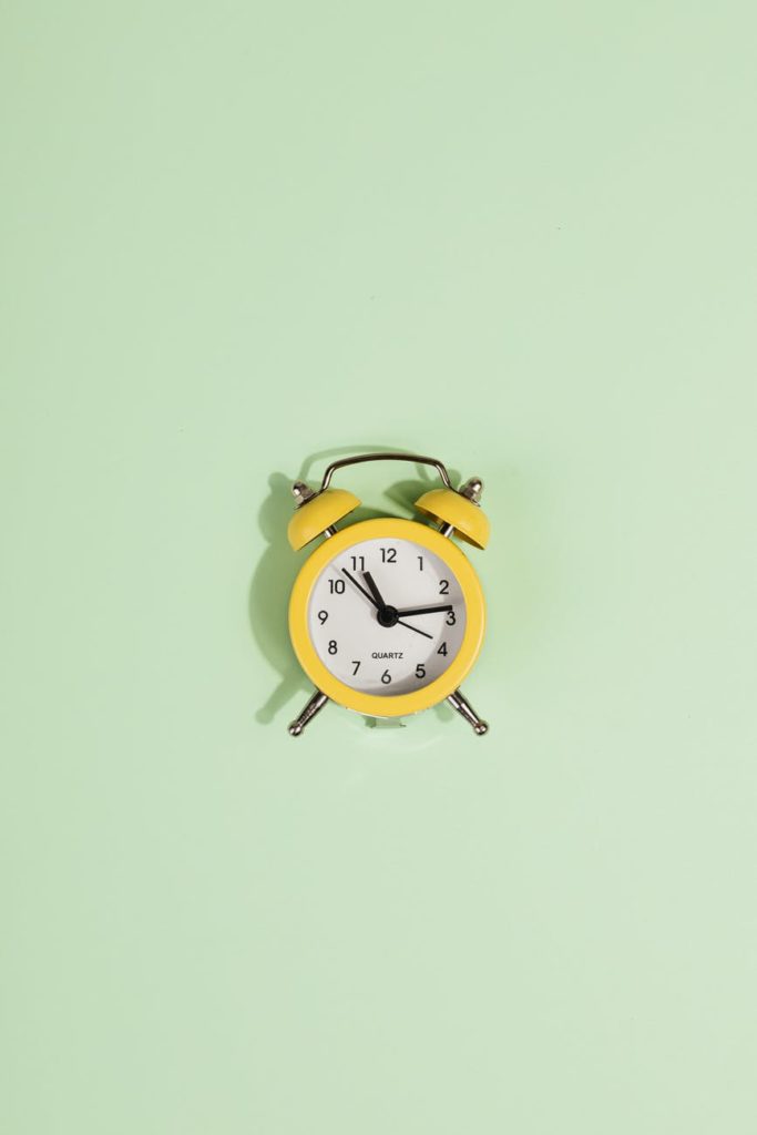 yellow alarm clock on green pastel background